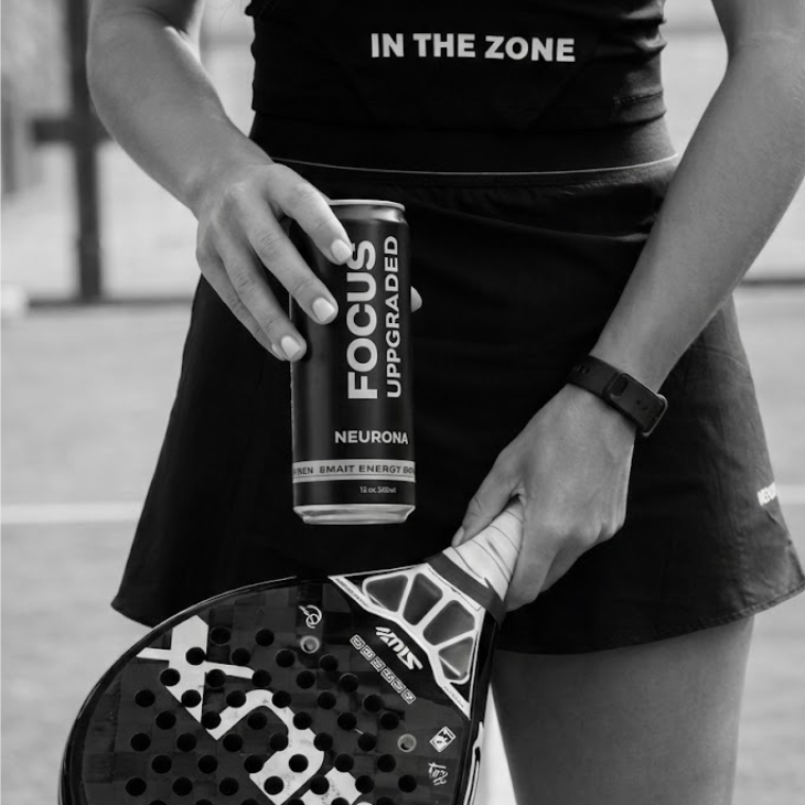 Person holding a paddle and a can of 'Focus Upgraded' on a sports court.
